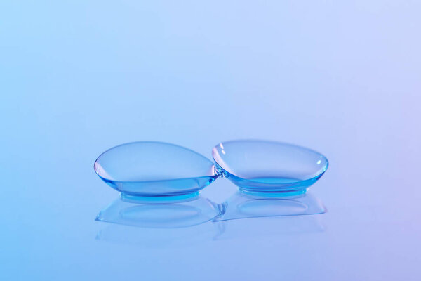 Pair of contact lenses and water drops on blue gradient mirror surface, closeup