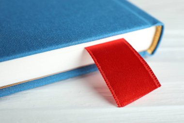 Beyaz ahşap masa üzerinde kırmızı kurdele yer imi olan kitap, yakın plan.