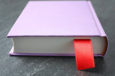 Koyu desenli masa üzerinde kırmızı kurdele yer imi olan kitap, yakın plan.