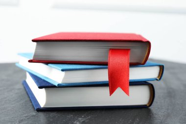 Kırmızı kurdele yer imi ve koyu dokulu masa üzerindeki renkli kitaplarla aydınlık arkaplan, yakın plan