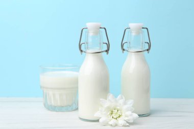 Açık mavi arka planda beyaz masada taze süt ve çiçek