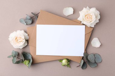 Boş tebrik kartı, kağıt zarflar, gül çiçekleri ve bej arka planda okaliptüs dalları, düz uzanma