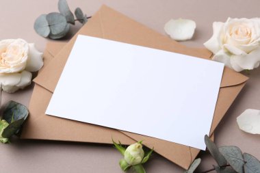 Boş tebrik kartı, kağıt zarflar, gül çiçekleri ve bej arka planda okaliptüs dalları, yakın plan.