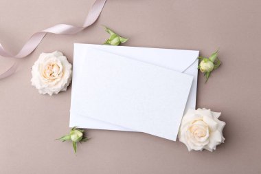 Boş tebrik kartı, kağıt zarf ve bej arka planda gül çiçekleri, düz uzanma
