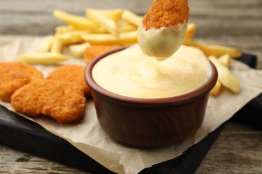 Tavuk nuggetını ahşap masada peynir sosuna batırmak, yakın plan.