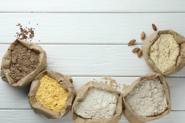 Beyaz ahşap masadaki kağıt torbalarda farklı türde un, düz bir şekilde. Metin için boşluk