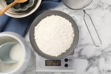 Beyaz mermer masa üzerinde bir kase un ve diğer ürünlerle birlikte dijital mutfak terazisi.