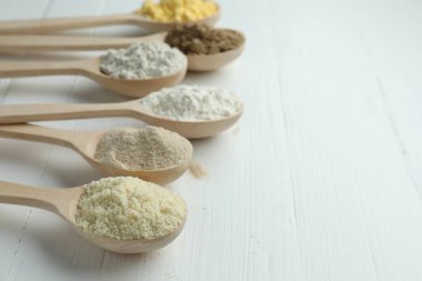 Beyaz ahşap masadaki kaşıklarda farklı türde un, yakın plan. Metin için boşluk