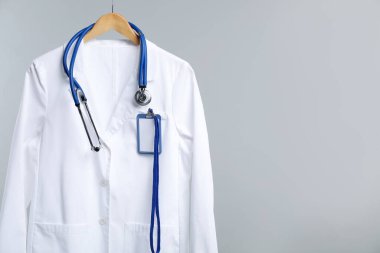 Üzerinde steteskop ve rozet olan doktor ceketi gri arka planda. Metin için boşluk