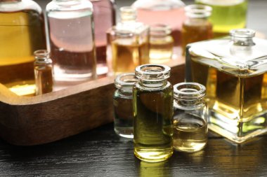 Siyah ahşap arka planda aromatik yağlı parfüm şişeleri, yakın plan.