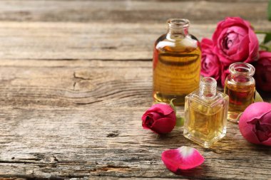 Ahşap masanın üzerinde aromatik esanslı yağlar ve güller olan parfüm şişelerini aç, yakın plan. Metin için boşluk