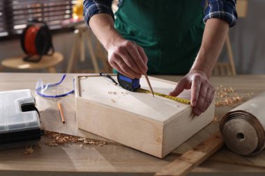 İçerideki masada bant ve kalemle ahşap kutuyu ölçen adam, yakın plan.