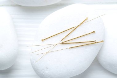 Akupunktur iğneleri ve spa taşları beyaz masada, yakın plan.