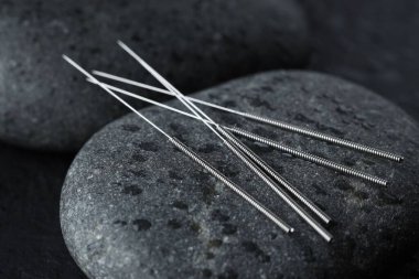 Akupunktur iğneleri ve karanlık arka planda ıslak spa taşları, yakın plan.