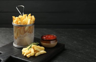 Lezzetli patates kızartması, ketçap ve biberiyeyle servis ediliyor, siyah masada, yakın plan. Metin için boşluk