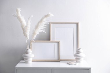 Beyaz duvarın yanındaki dolapta boş resim çerçeveleri ve şık ev dekorasyonu