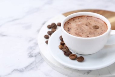 Aromatik kahve fincanda, fasulye ve çay tabağı beyaz mermer masada, yakın plan. Metin için boşluk