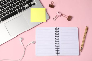 Not defteri, yapışkan not, kalem, klasör klipleri, kulaklıklar ve pembe arka planda dizüstü bilgisayarlar.