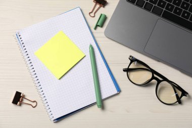 Not defteri, yapışkan not, kalem, gözlük, cilt klipsleri ve dizüstü bilgisayar ahşap masa, düz yatıyordu.