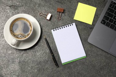 Not defteri, kalem, yapışkan not, kahve, cilt klipsleri, ve gri masada dizüstü bilgisayar, düz konum