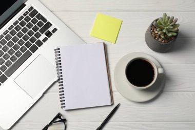 Not defteri, kalem, yapışkan not, kahve, çiçekli dekor ve dizüstü bilgisayar beyaz ahşap masa, düz yatıyordu.