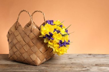 Mercan zeminine karşı ahşap masanın üzerinde güzel çiçekler olan hasır sepet. Metin için boşluk