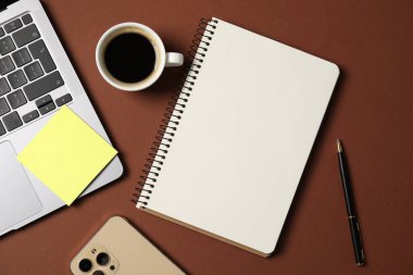 Kalem, dizüstü bilgisayar, akıllı telefon, kahverengi arka planda yapışkan not ve kahve içeren defter, düz konum