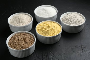 Siyah desenli masa üzerindeki kaselerde farklı un türleri, yakın plan.