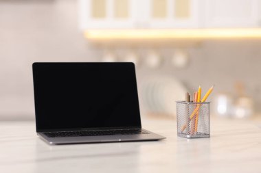 Boş ekranlı dizüstü bilgisayar ve mutfaktaki beyaz mermer masada kırtasiye malzemesi. Tasarım için model