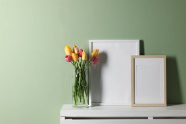 Boş resim çerçeveleri ve beyaz rafta soluk yeşil duvarın yanında güzel laleler.