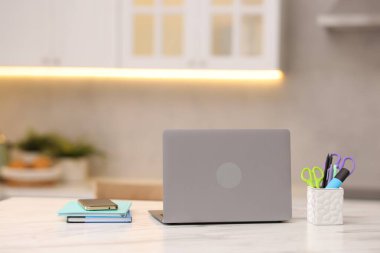 Laptop, akıllı telefon ve kırtasiye malzemeleri mutfaktaki beyaz mermer masada.