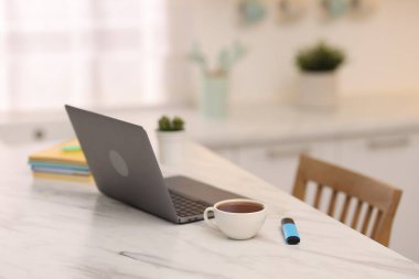 Laptop, kırtasiye malzemeleri ve bir fincan sıcak içecek mutfaktaki beyaz mermer masada, seçici bir odak noktası