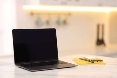 Boş ekranlı dizüstü bilgisayar, akıllı telefon ve kırtasiye malzemesi mutfaktaki beyaz mermer masada. Tasarım için model
