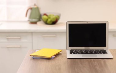 Boş ekranlı dizüstü bilgisayar ve mutfaktaki ahşap masada defterler. Tasarım için model