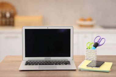 Boş ekranlı dizüstü bilgisayar, akıllı telefon ve mutfaktaki ahşap masada kırtasiye malzemesi. Tasarım için model