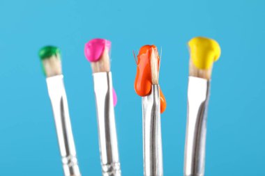 Açık mavi arkaplanda renk boyalı birçok fırça, yakın plan