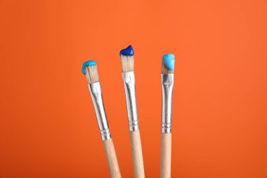 Turuncu arka planda renkli üç fırça, yakın plan.