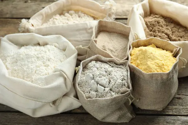 Tahta masadaki poşetlerdeki farklı un türleri, yakın plan.