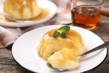 Karamel soslu lezzetli puding ve ahşap masada servis edilen nane, yakın plan.
