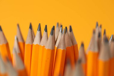 Many graphite pencils on orange background, closeup
