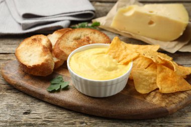 Lezzetli peynir sosu kaseye, nacho cipsi ve ekmek kırıntıları ahşap masaya, yakın plan.