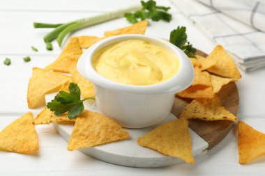 Lezzetli bir peynir sosu ve beyaz ahşap masada nacho cipsi, yakın plan.