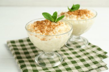 Tarçınlı lezzetli sütlaç ve beyaz masadaki cam tatlı kaselerinde naneli şeker.