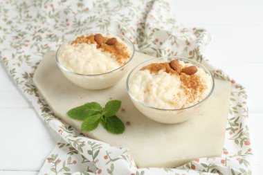 Tarçınlı lezzetli pirinç pudingi, beyaz ahşap masada nane ve badem, yakın plan.