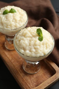 Cam tatlı kaselerinde naneli sütlaç, siyah masada, yakın plan.