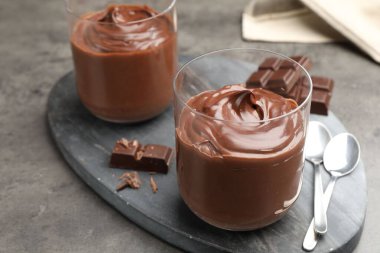 Lezzetli puding ve çikolata parçaları gri masada, yakın plan.