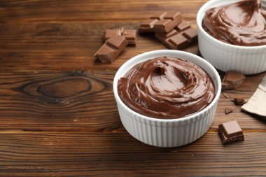 Tabaklardaki lezzetli pudingler ve ahşap masadaki çikolata parçaları, metin için yer.