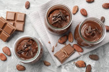 Cam kavanozlarda lezzetli puding, çikolata ve kakao çekirdekleri açık gri masada, düz yatıyordu.