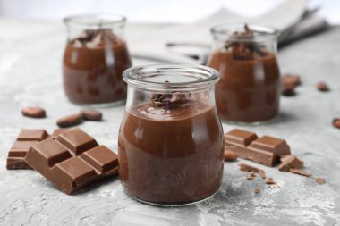 Cam kavanozlarda lezzetli puding ve açık gri masada çikolata parçaları, yakın plan.