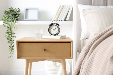 Alarmlı komodinli komodin, bir bardak su ve yatağın yanında kitap.